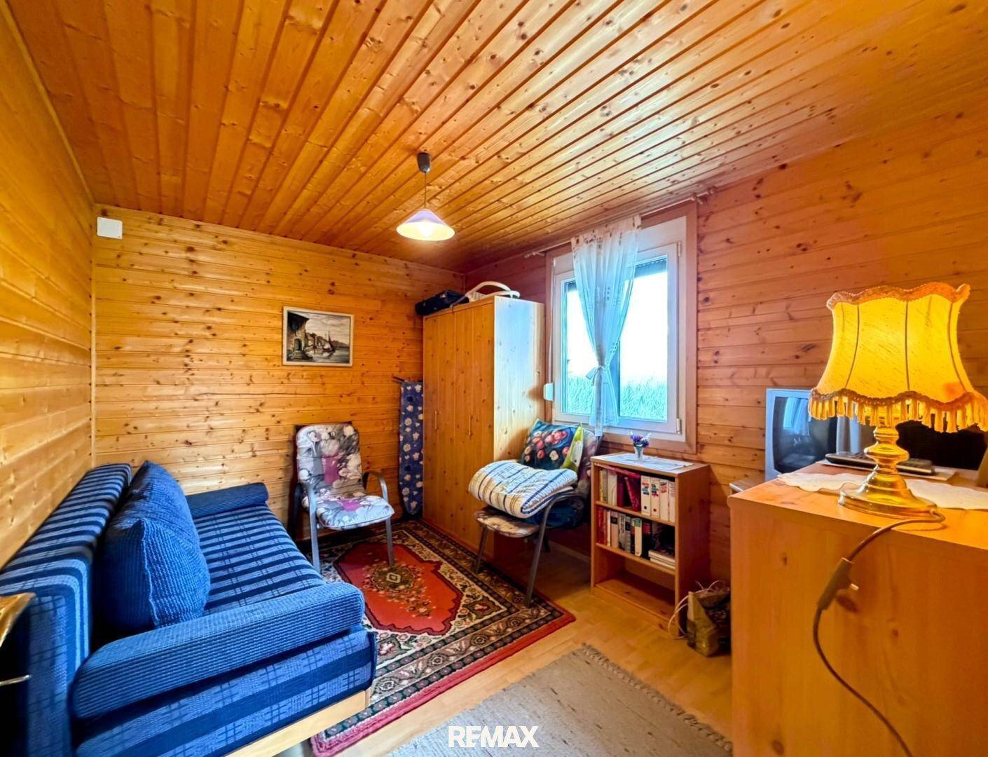 Weiteres Schlafzimmer mit einem blauen Sofa, Holzwänden und -decke, sowie einem kleinen Fenster.