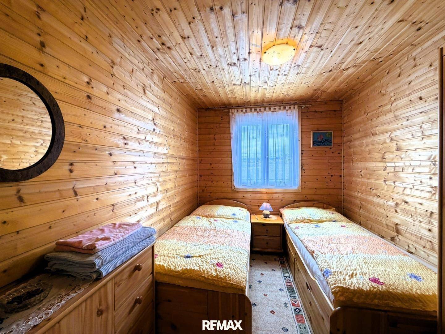 Gemütliches Schlafzimmer mit zwei Einzelbetten, Holzwänden und -decke, sowie einem Fenster.