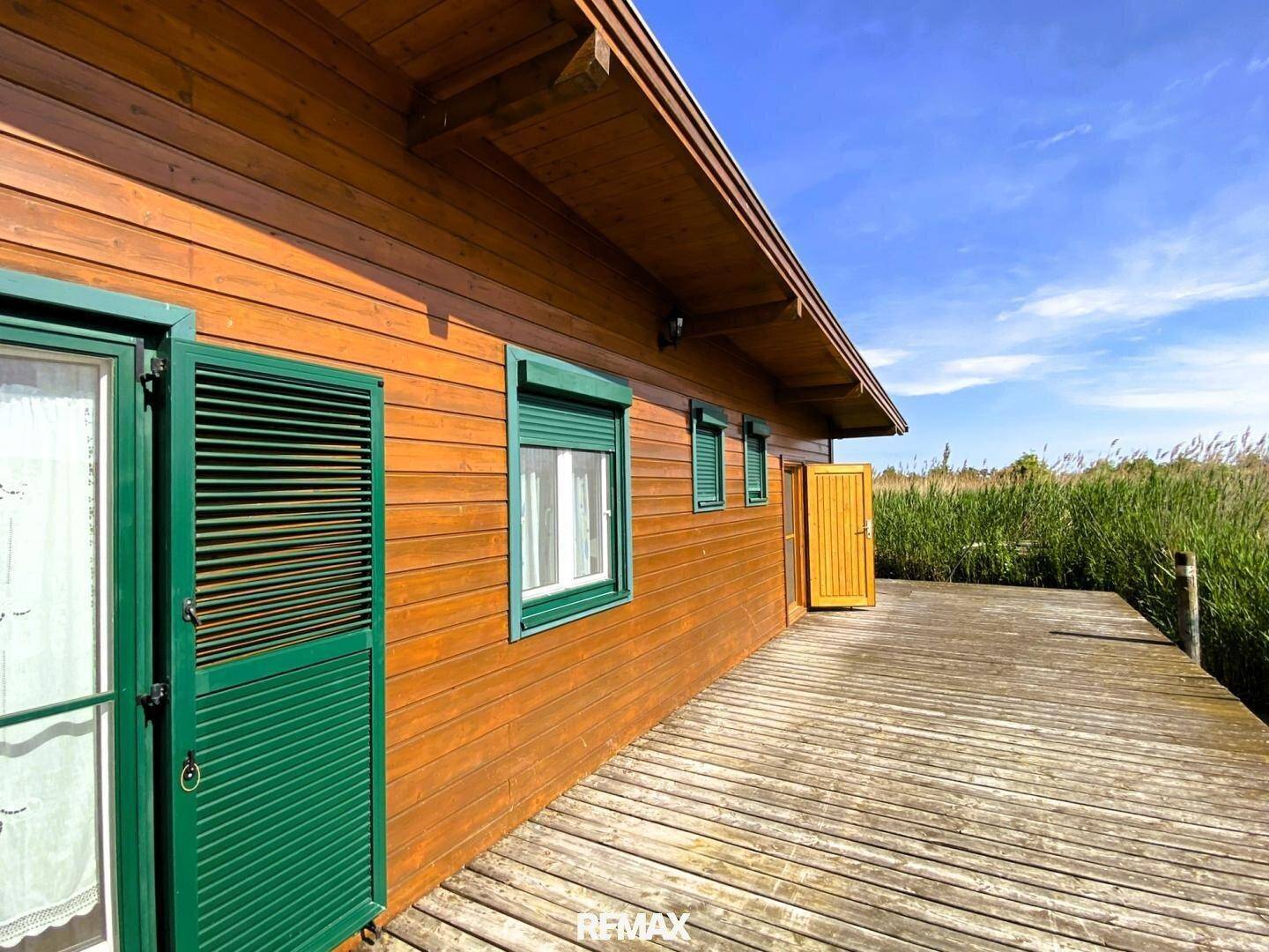 Seitenansicht des Holzhauses mit grünen Fensterläden und einer langen Holzterrasse am Wasser.