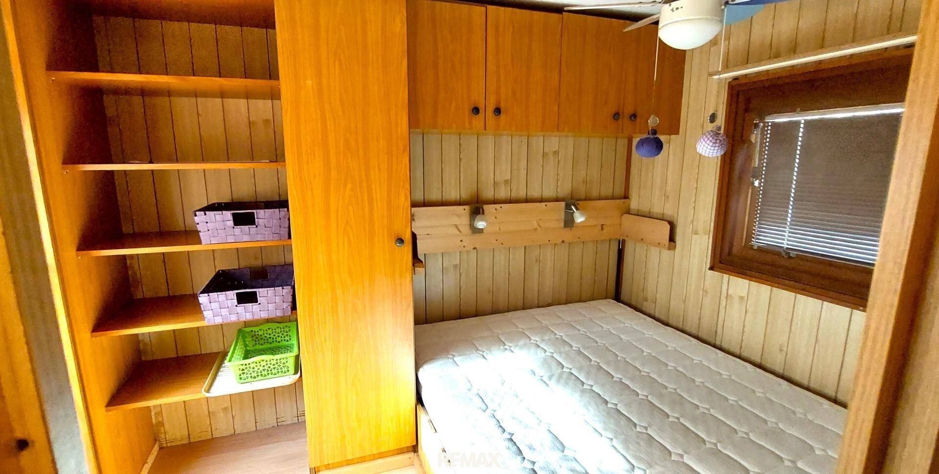 Schlafzimmer mit Einzelbett, Holzregalen und Deckenventilator, einfach und funktional eingerichtet.