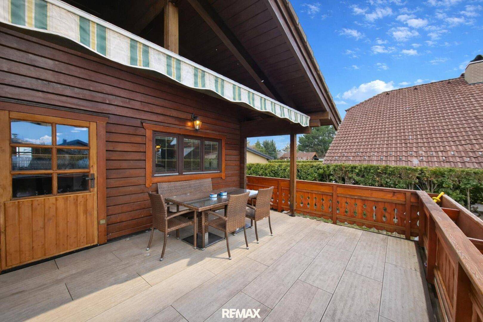 Überdachte Terrasse mit Holzboden, Esstisch und Markise für angenehme Stunden im Freien.