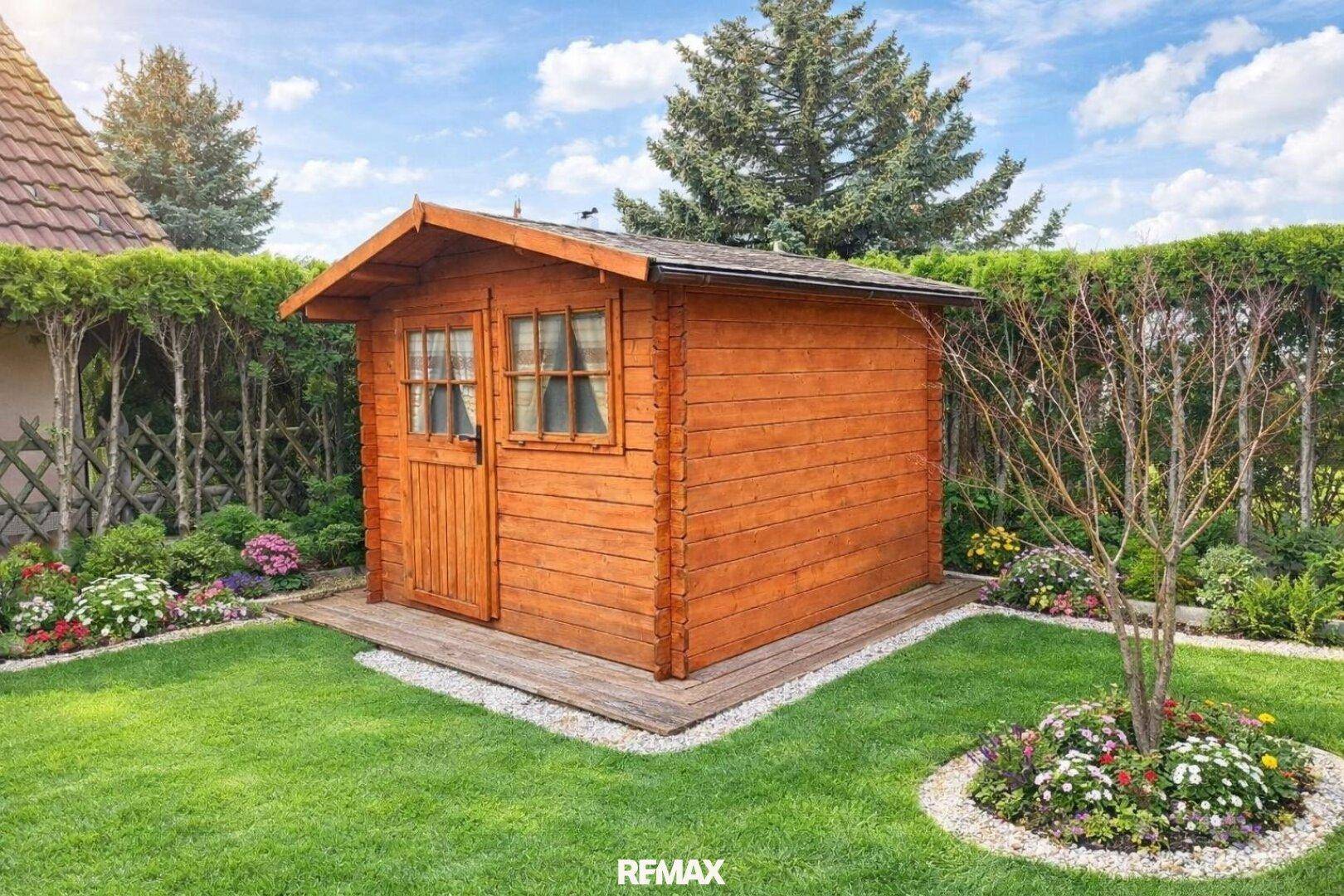 Charmantes Gartenhaus aus Holz, umgeben von Blumenbeeten und gepflegtem Rasen.