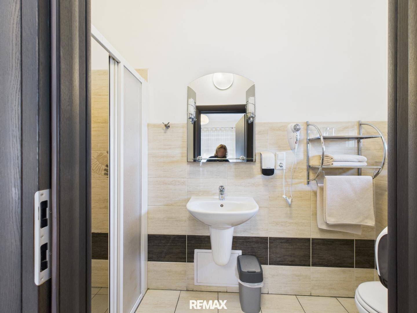 Kleines Badezimmer mit Duschkabine, Waschbecken und WC, gefliest in hellen und dunklen Farbtönen.