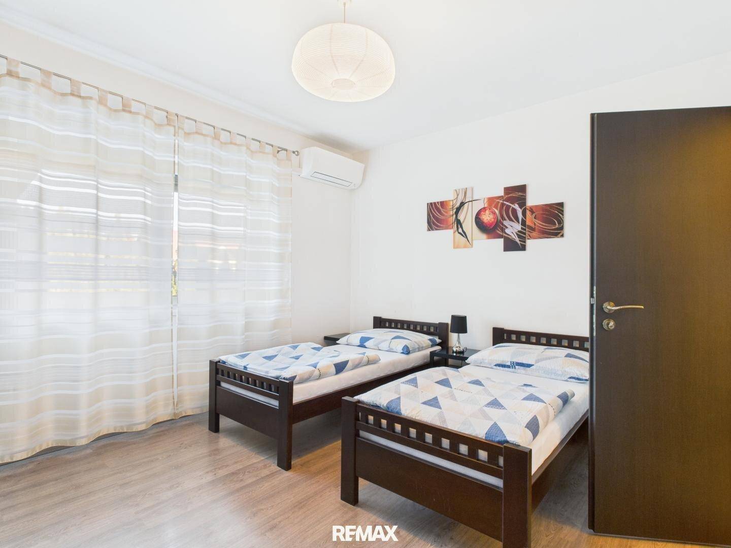 Schlafzimmer mit zwei Einzelbetten, Holzboden und einem Fenster mit Vorhängen für natürliches Licht.