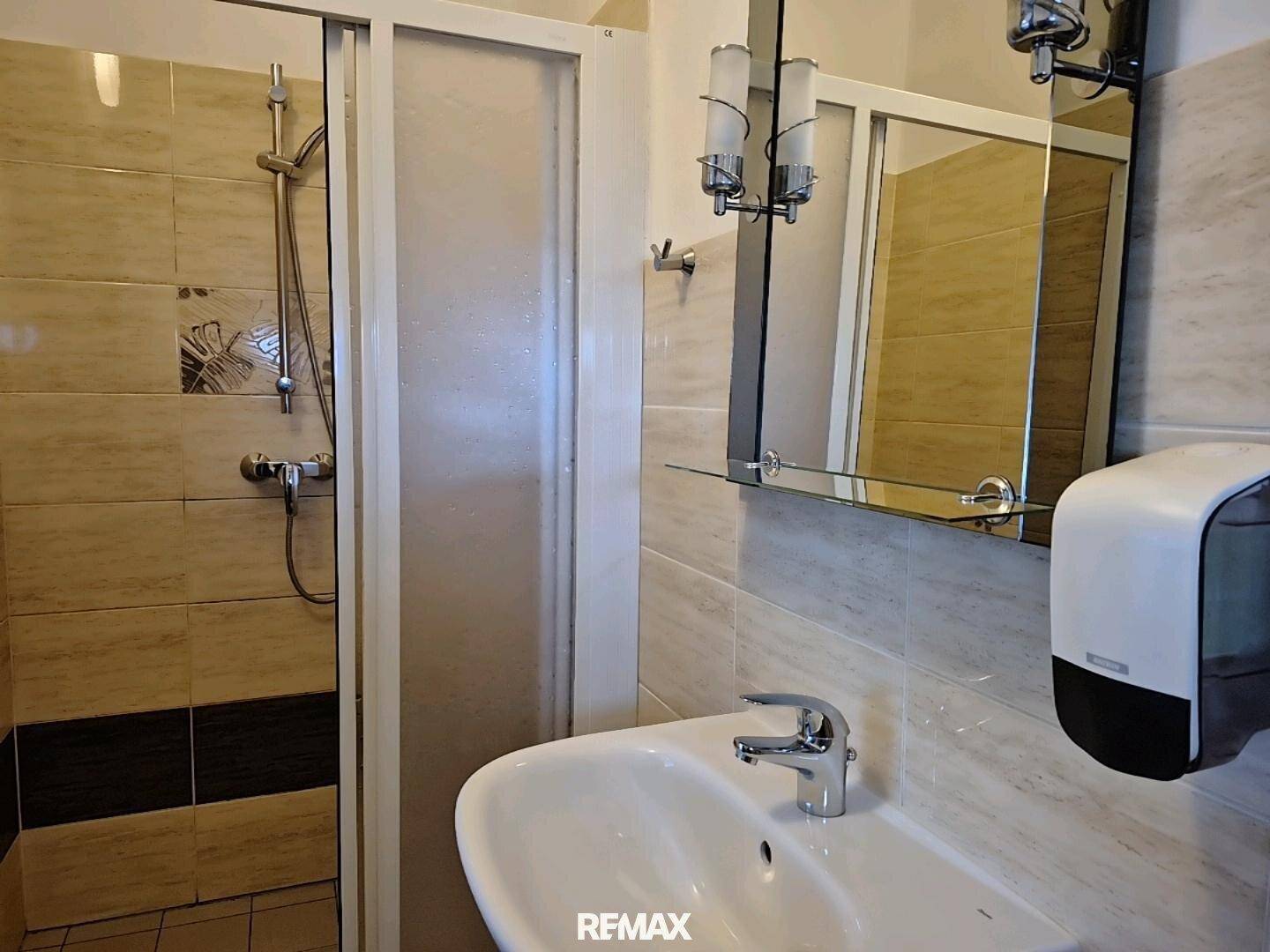 Badezimmer mit Duschkabine, Waschbecken und Spiegel, gefliest in beigen und braunen Farbtönen.