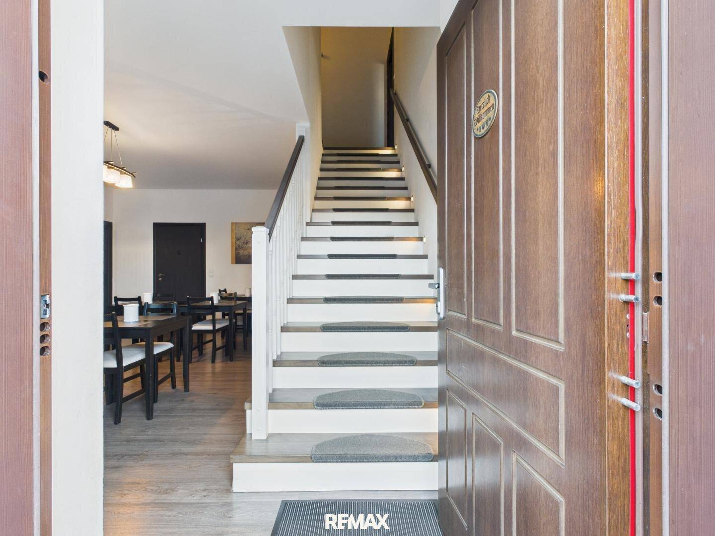 Eingangsbereich mit Holztür und Treppe, die in den oberen Stock führt, mit Blick auf den Essbereich.