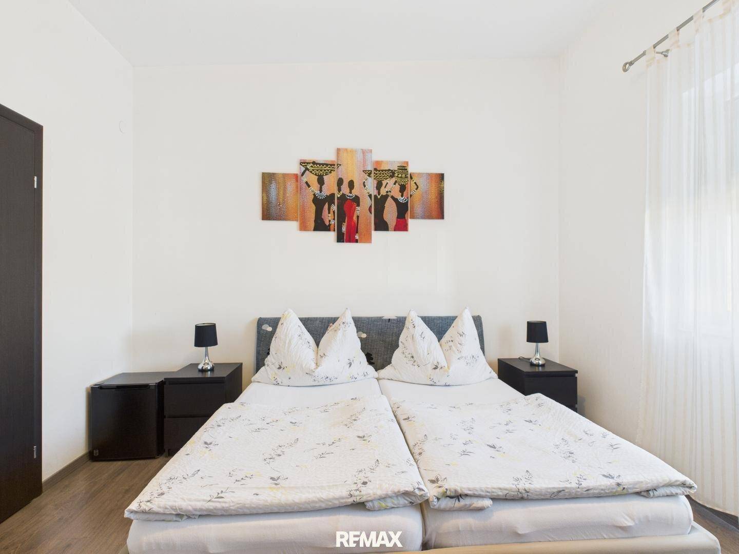 Helles Schlafzimmer mit zwei Einzelbetten, Holzboden und einem farbenfrohen Wandbild über dem Bett.