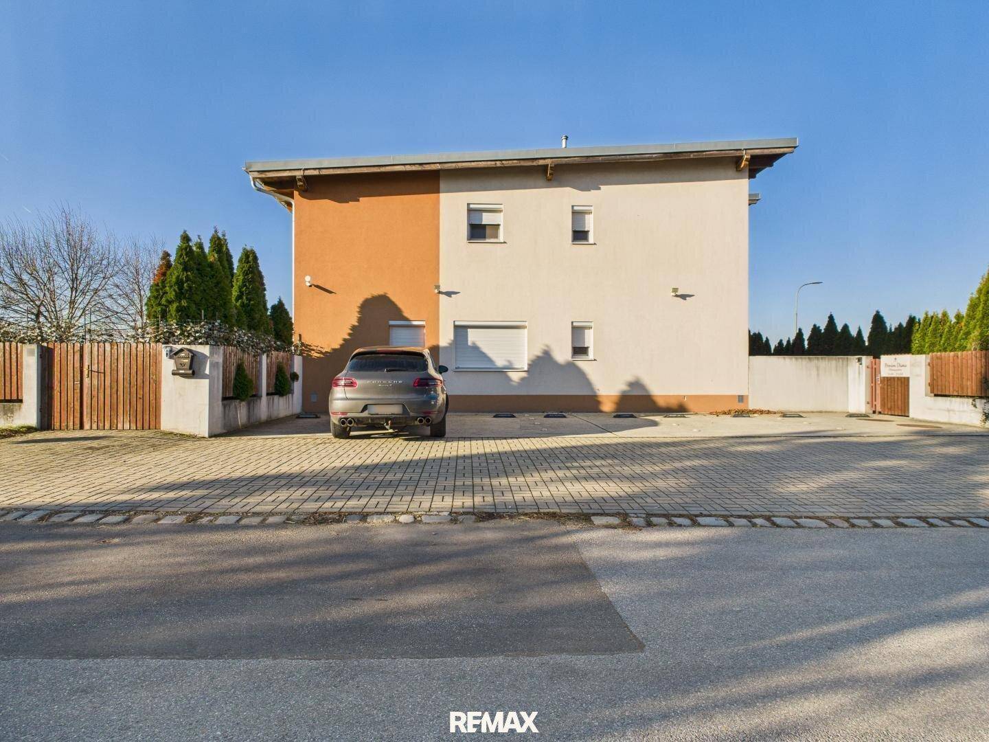 Seitenansicht des Hauses mit gepflasterter Einfahrt und einem geparkten Auto vor der Fassade.