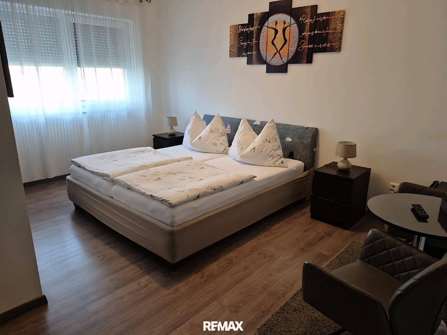 Gemütliches Schlafzimmer mit Doppelbett, Sitzgelegenheit und Fenster, geschmackvoll mit Wandbildern dekoriert.