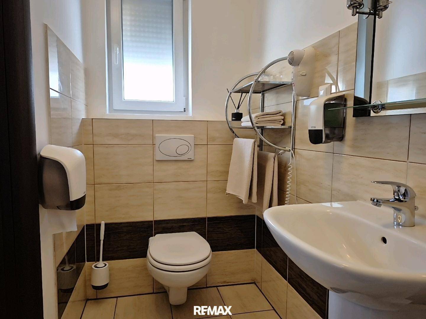Modernes Badezimmer mit WC, Waschbecken und Fenster, gefliest in hellen und dunklen Farbtönen.