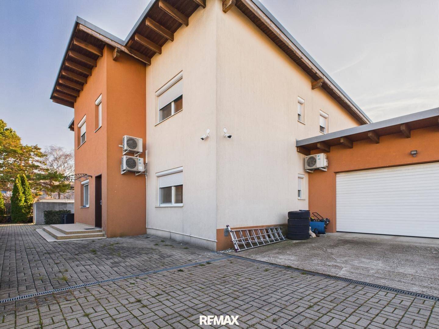 Seitenansicht des Hauses mit einer Garage und einem gepflasterten Vorplatz unter blauem Himmel.