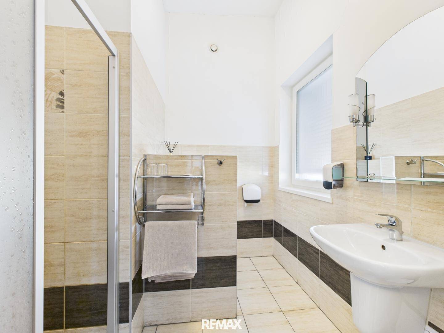 Modernes Badezimmer mit Duschkabine, Waschbecken und Fenster, gefliest in hellen und dunklen Tönen.