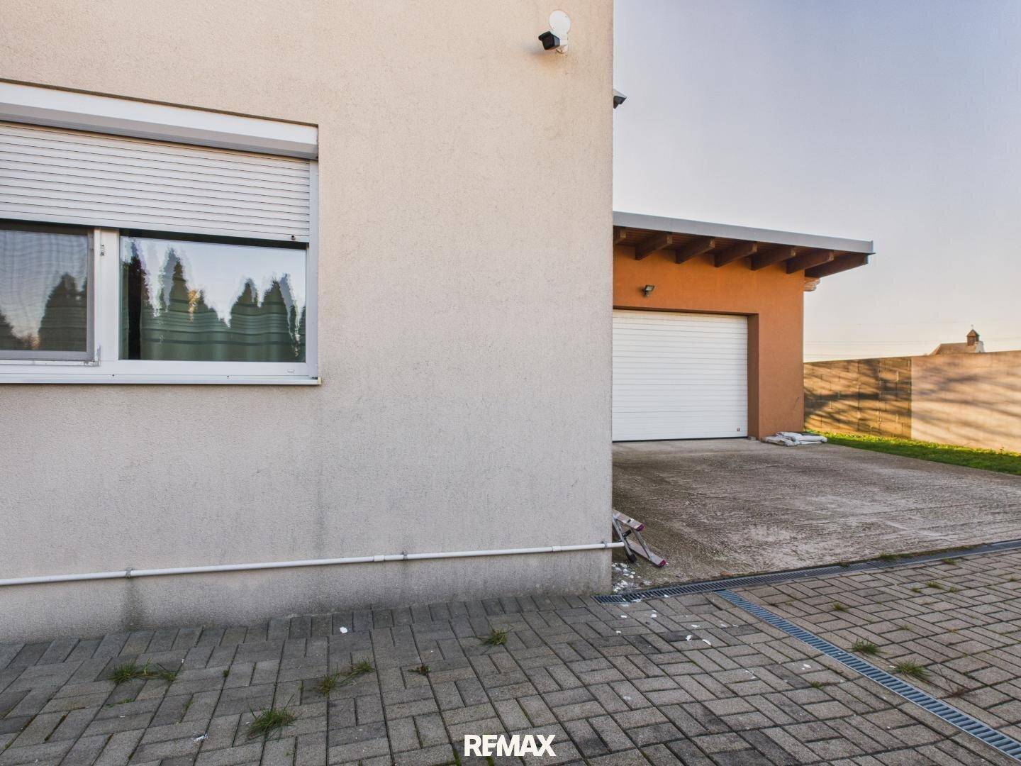 Nahaufnahme der Hausseite mit einer Garage und einem gepflasterten Bereich unter blauem Himmel.