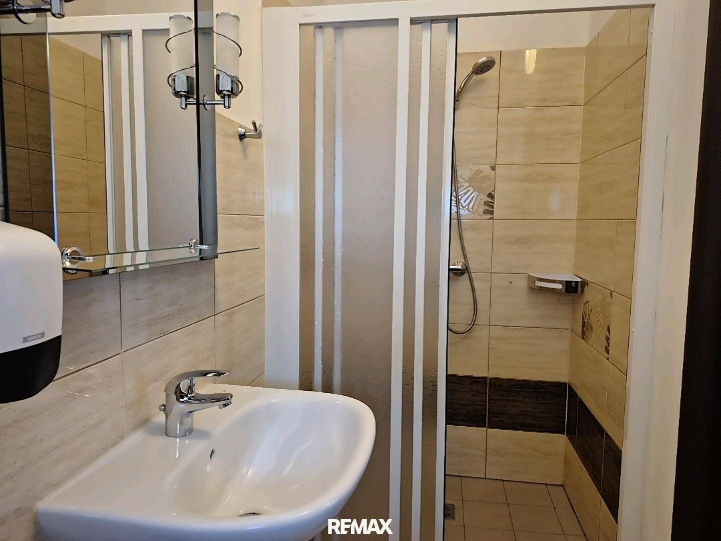 Badezimmer mit Duschkabine und Waschbecken, gefliest in beigen und braunen Tönen, mit Spiegel.