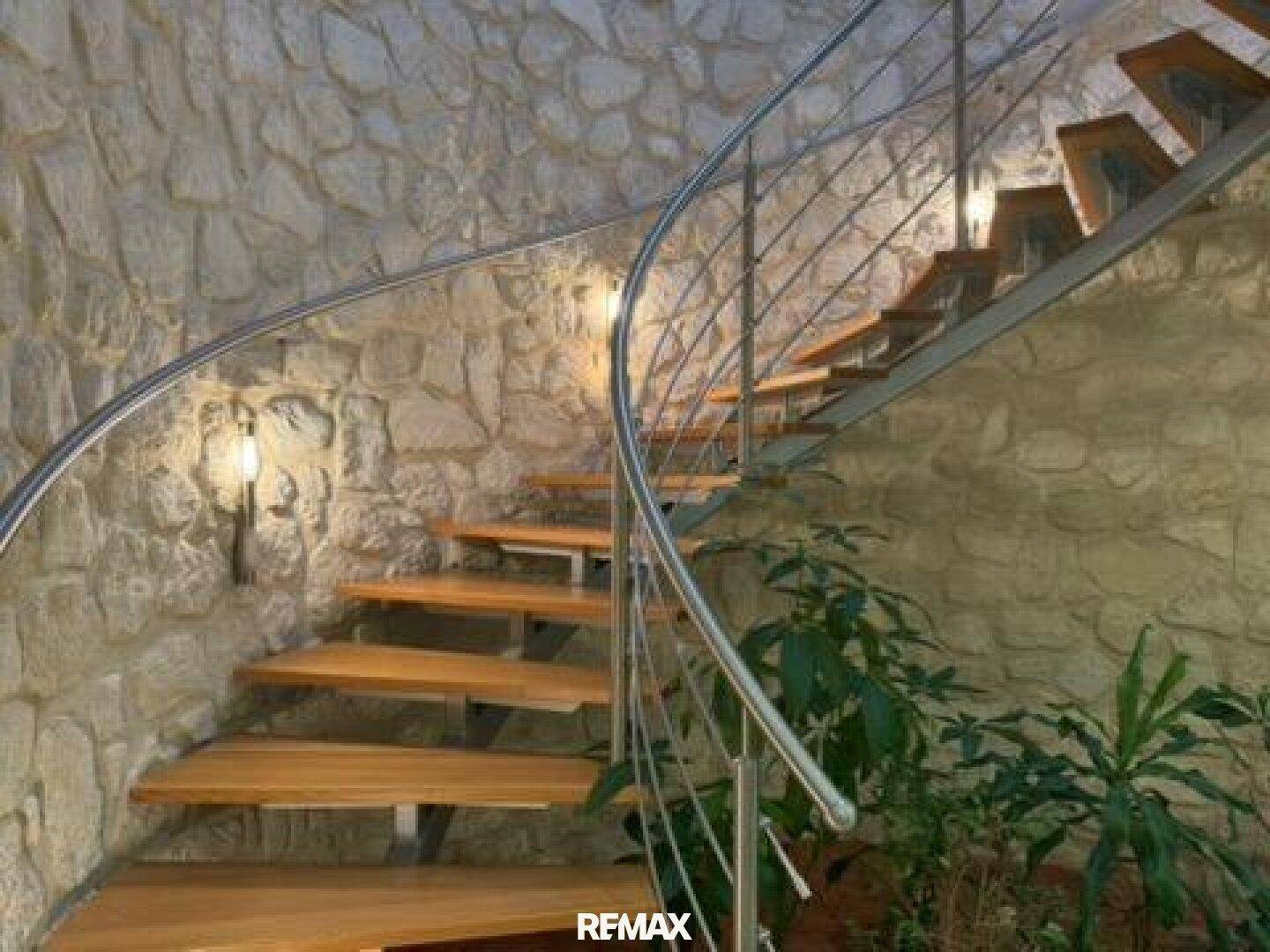 Detailansicht der eleganten Wendeltreppe mit Holzstufen und Metallgeländer vor der Natursteinwand.