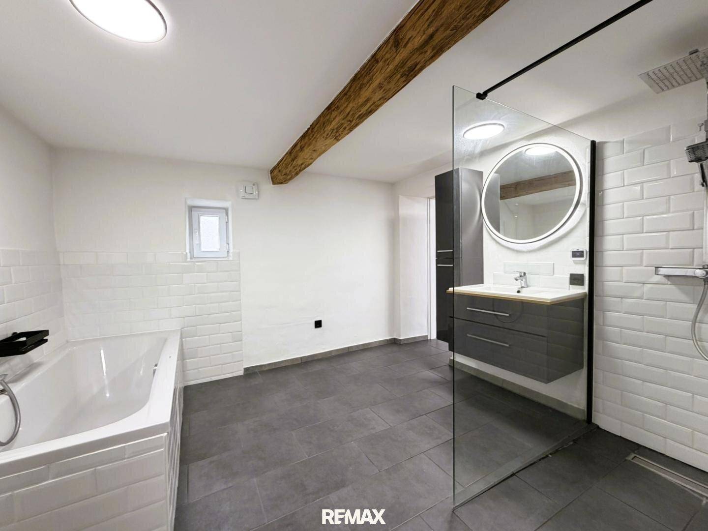 Modernes Badezimmer mit dunklen Fliesen, Badewanne, begehbarer Dusche und Waschtisch mit Spiegel.