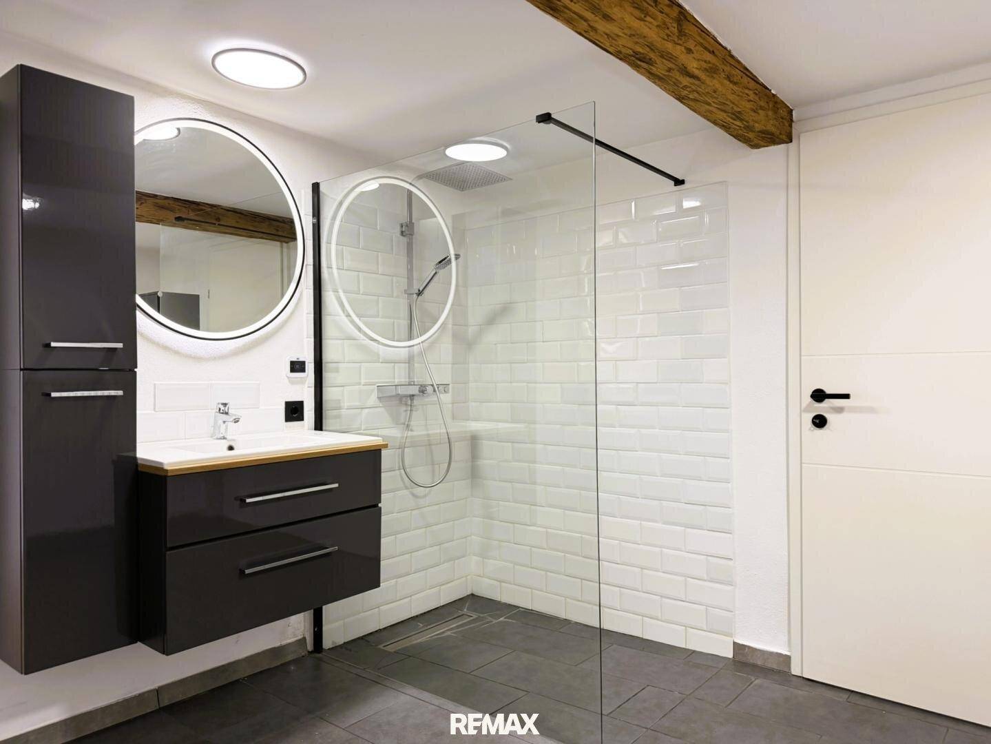 Stilvolles Badezimmer mit modernem Waschtisch, beleuchtetem Spiegel und großer begehbarer Dusche.