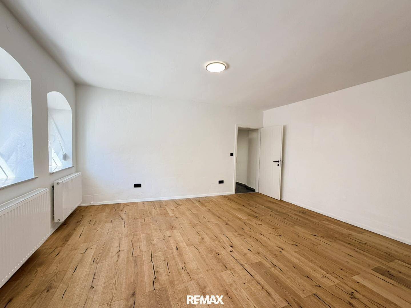 Heller Raum mit Holzboden und weißen Wänden, betont durch die tiefen Fensterlaibungen.