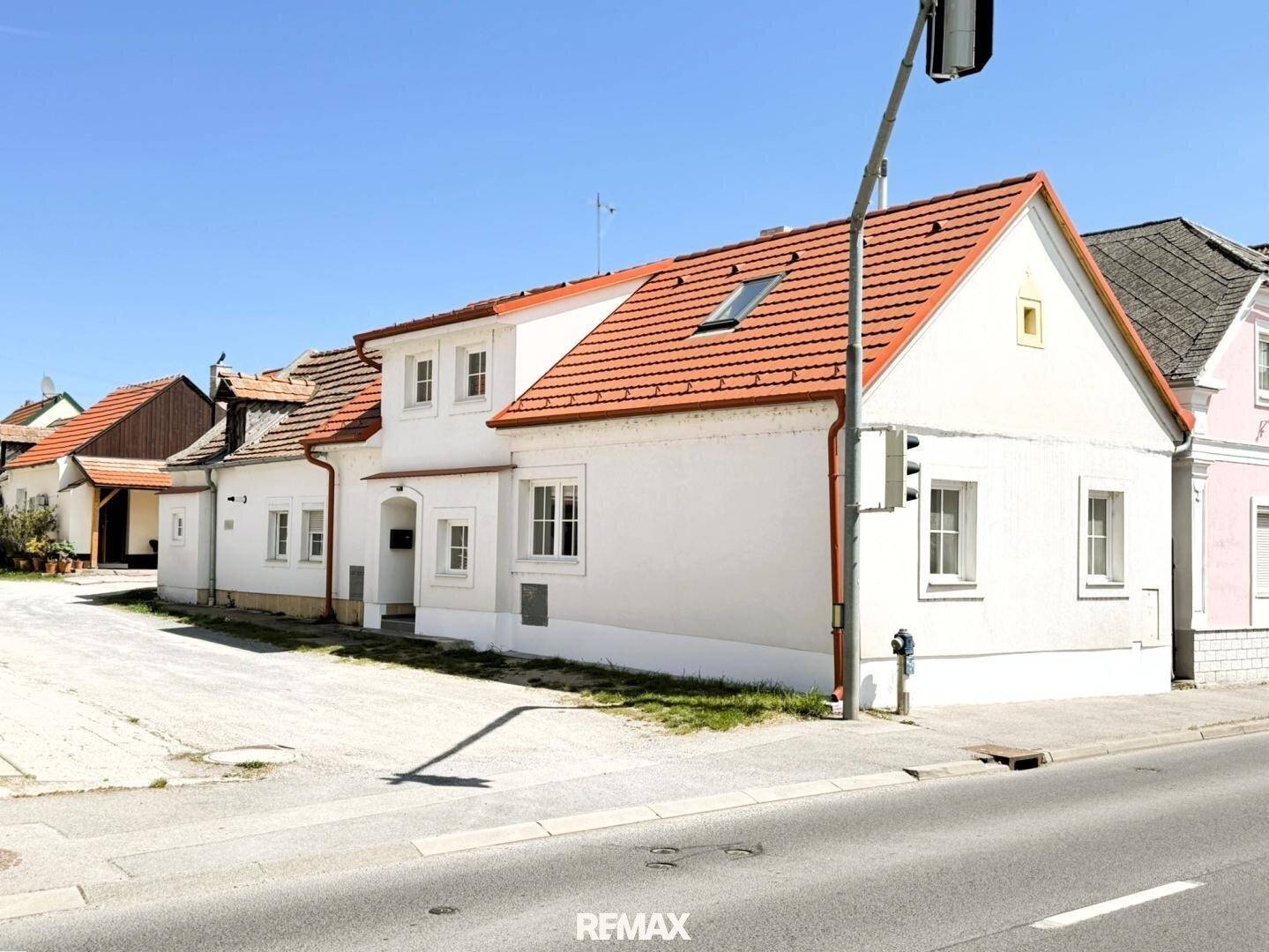 Ansicht des weißen Hauses mit rotem Ziegeldach und Dachfenster von der Straßenseite.