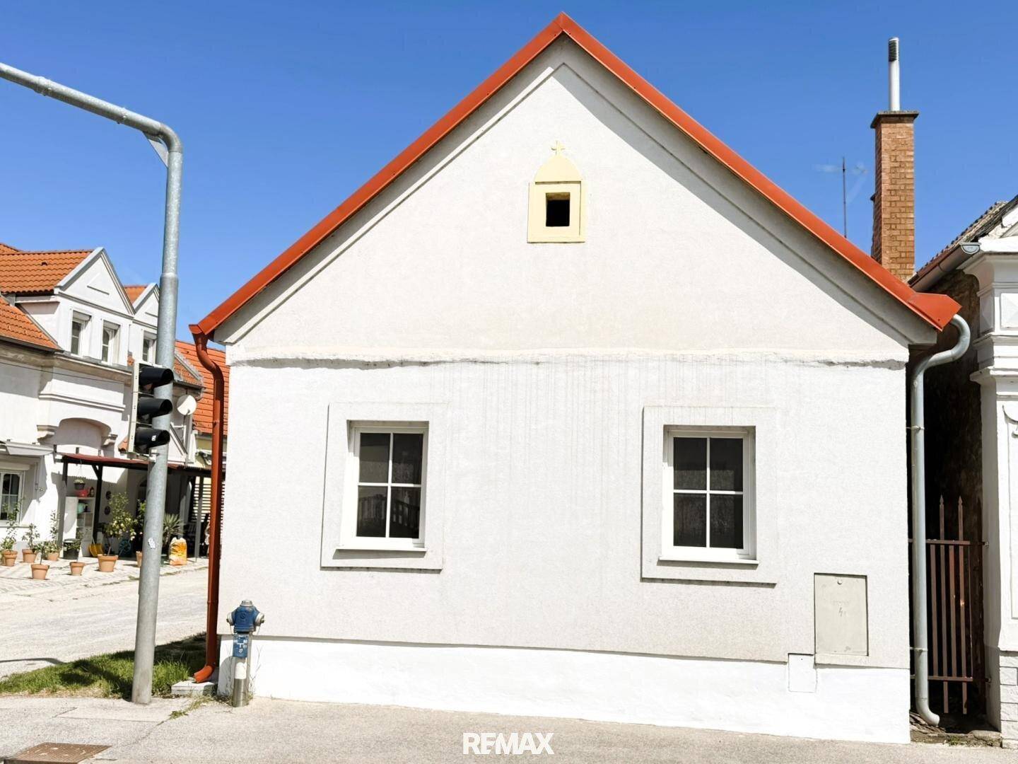 Seitenansicht des weißen Hauses mit Giebel, zwei Fenstern und einem Schornstein.