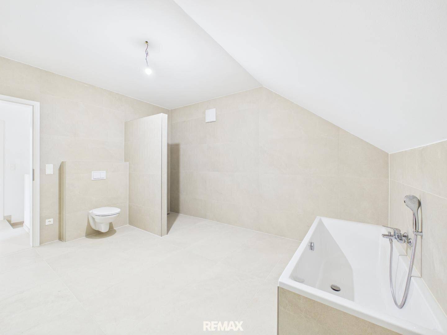 Modernes Badezimmer im Dachgeschoss mit Badewanne, Wand-WC und hellen Fliesen.