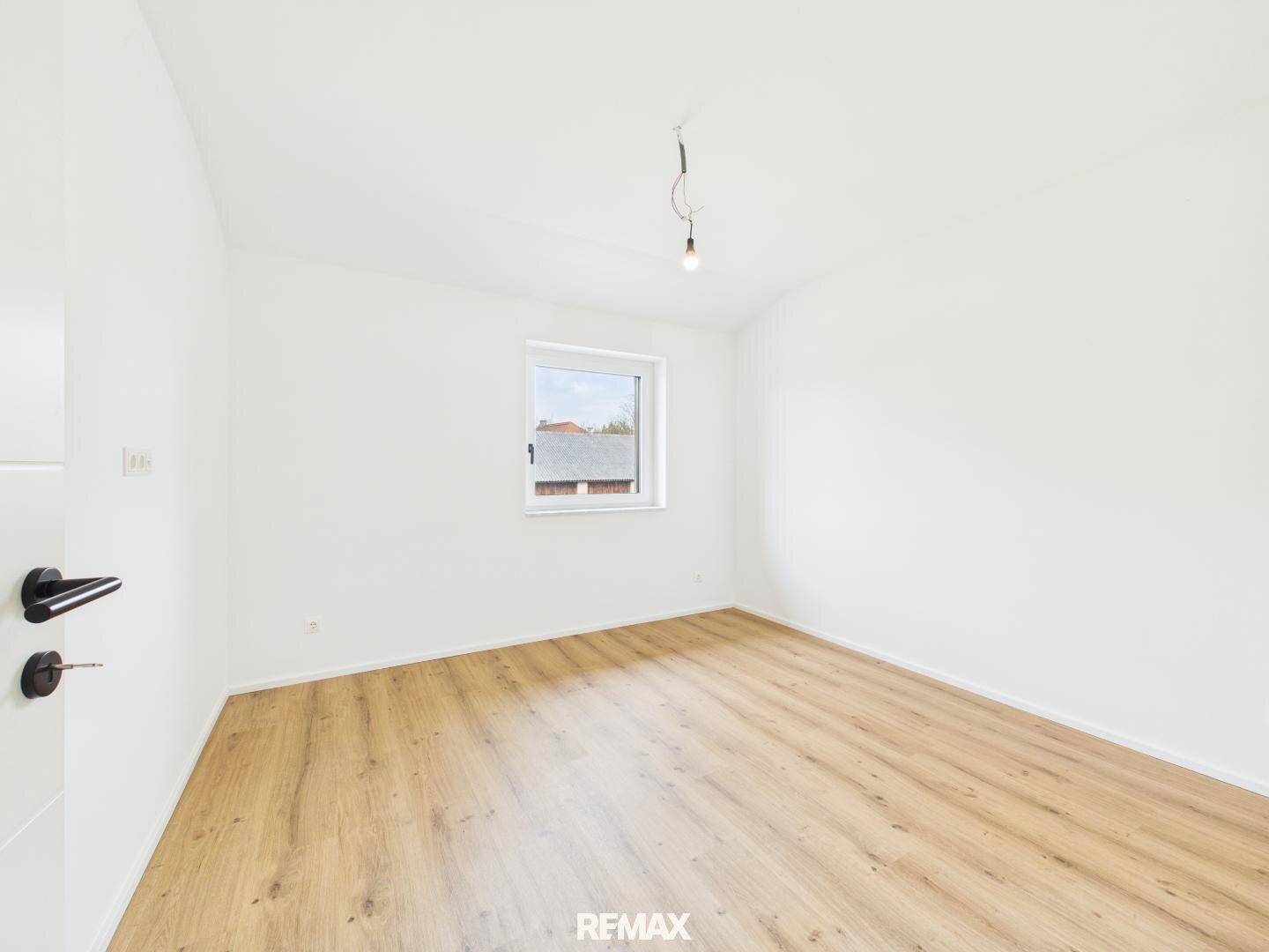 Leeres Schlafzimmer mit Holzboden, weißen Wänden und einem Fenster.