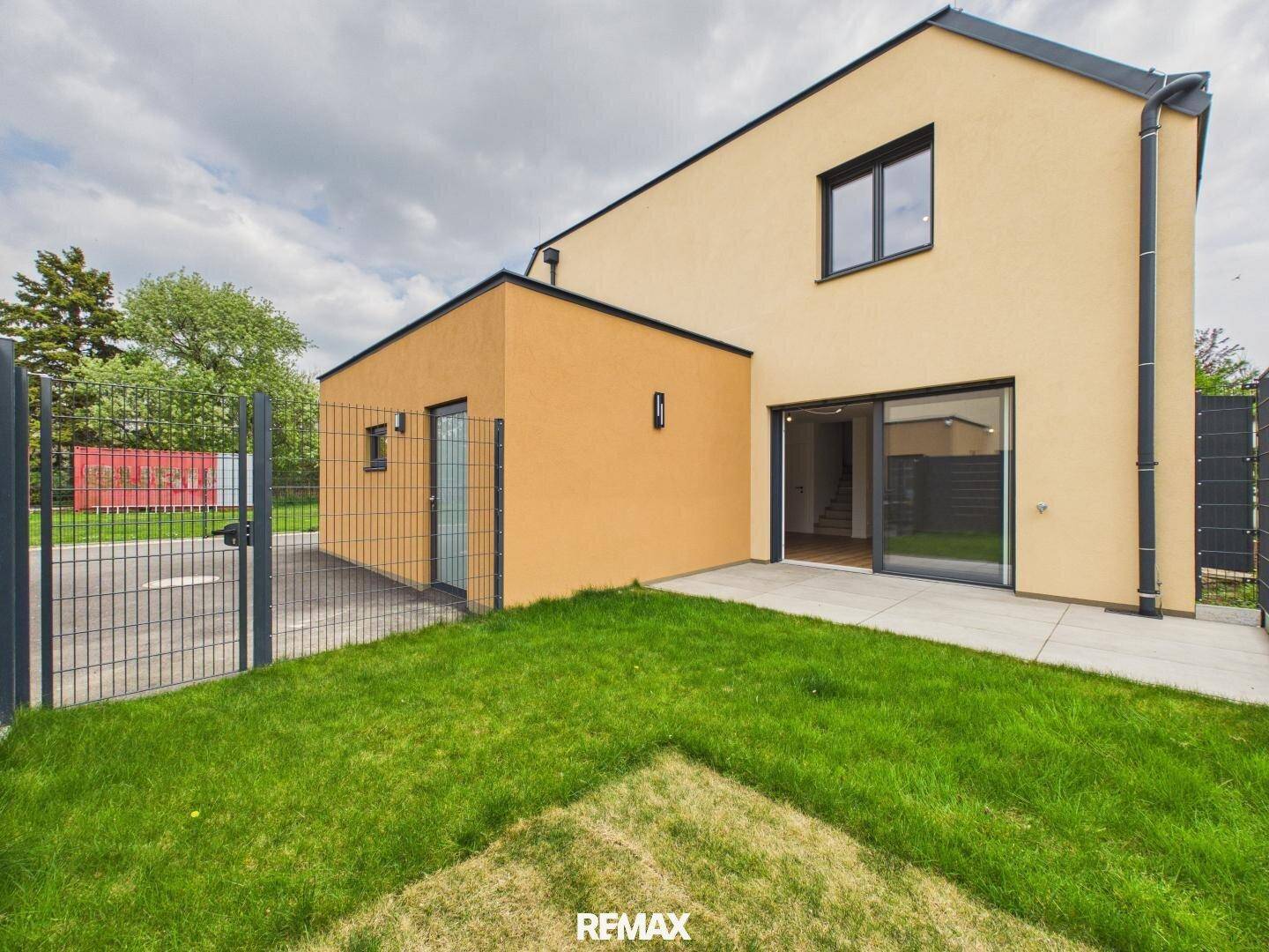 Gepflegte Rasenfläche und gepflasterter Bereich neben dem modernen Reihenhaus.