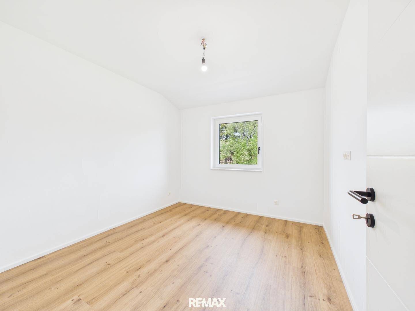 Helles Schlafzimmer mit Holzboden, weißen Wänden und Blick ins Grüne.