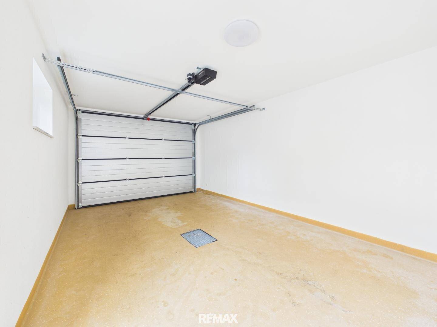 Leere Garage mit automatischem Tor, Fenster und einfachem Betonboden.