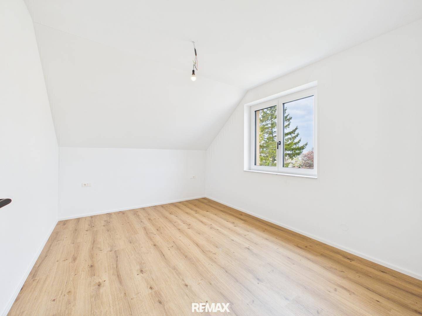 Helles Zimmer im Dachgeschoss mit Holzboden, weißen Wänden und Fenster.