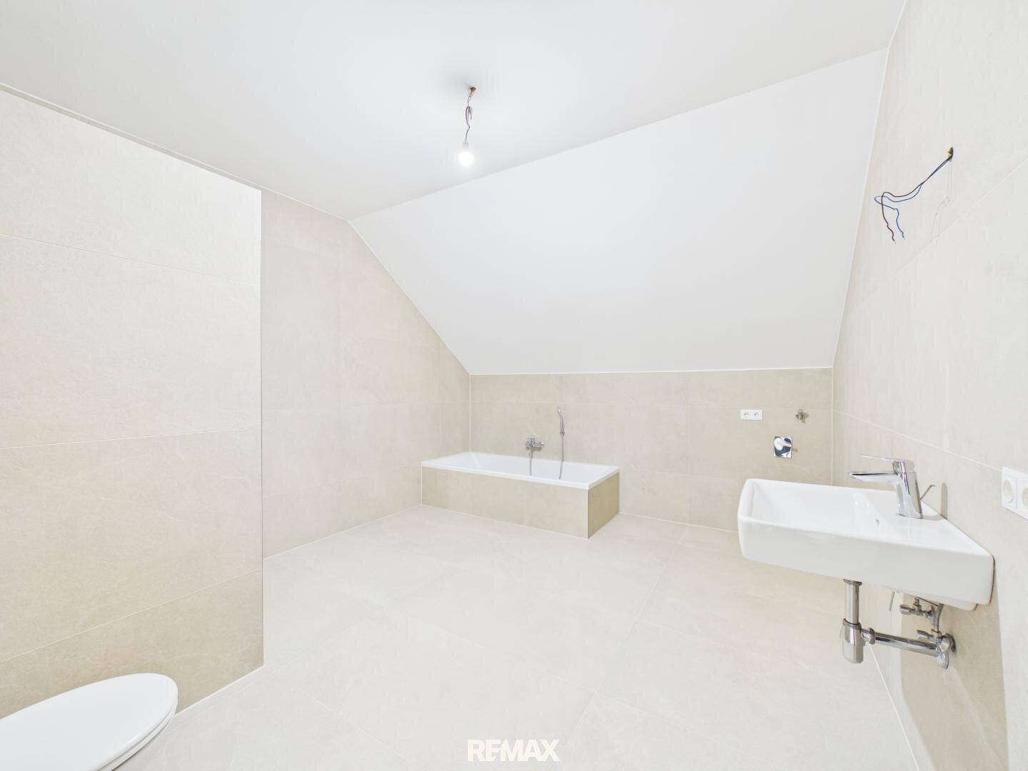 Geräumiges Badezimmer im Dachgeschoss mit Badewanne, Waschbecken und hellen Fliesen.