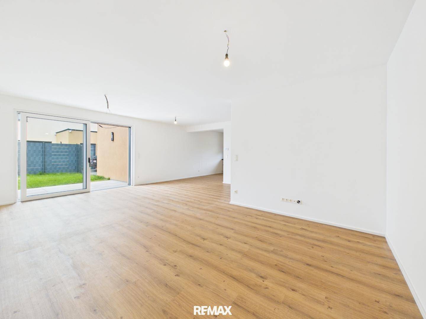 Heller, leerer Wohnbereich mit Holzboden und großzügigem Zugang zum Garten.