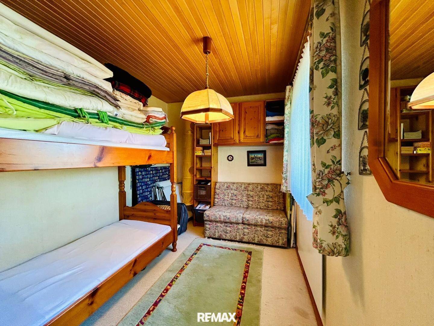 Kleines Schlafzimmer mit Etagenbett, Holzdecke und floralen Vorhängen.