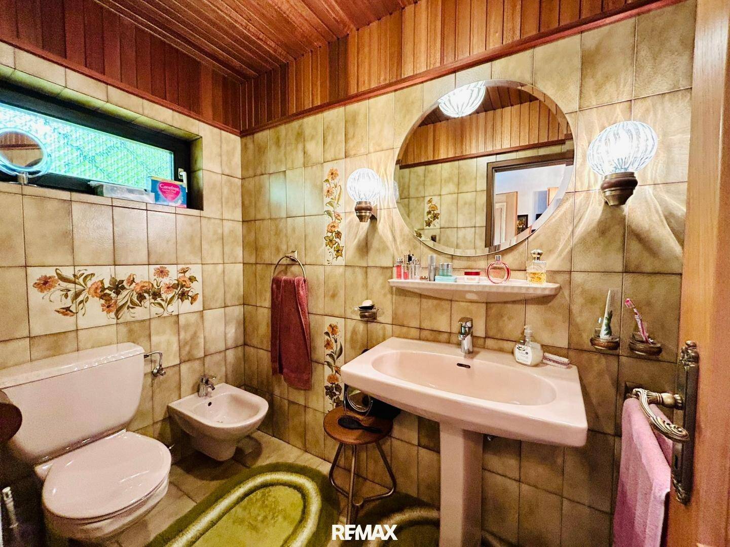 Badezimmer im 80er-Jahre-Stil mit rosa Waschbecken, Bidet und gemusterten Fliesen.