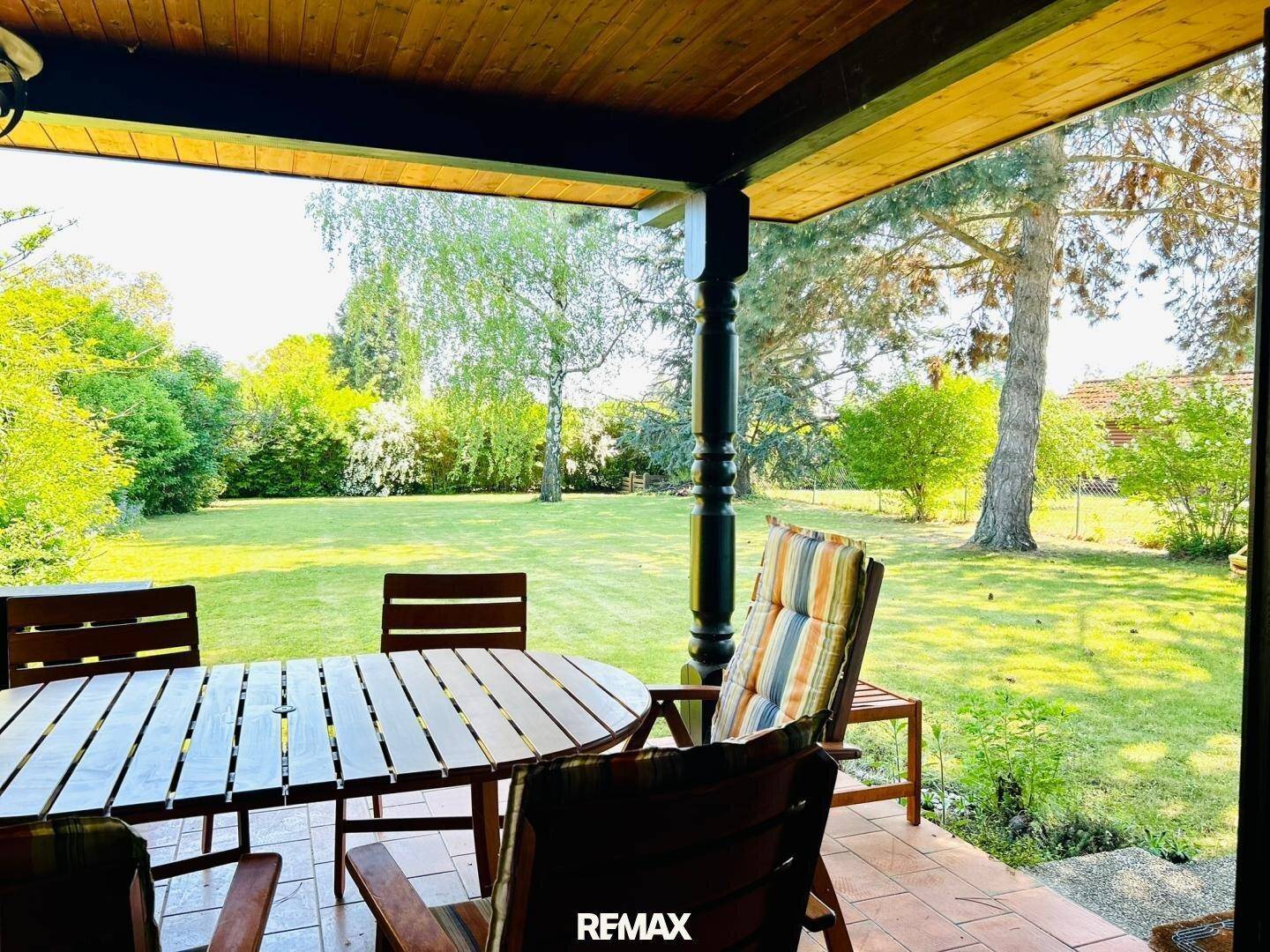 Blick von der überdachten Terrasse in den weitläufigen, sonnigen Garten mit altem Baumbestand.