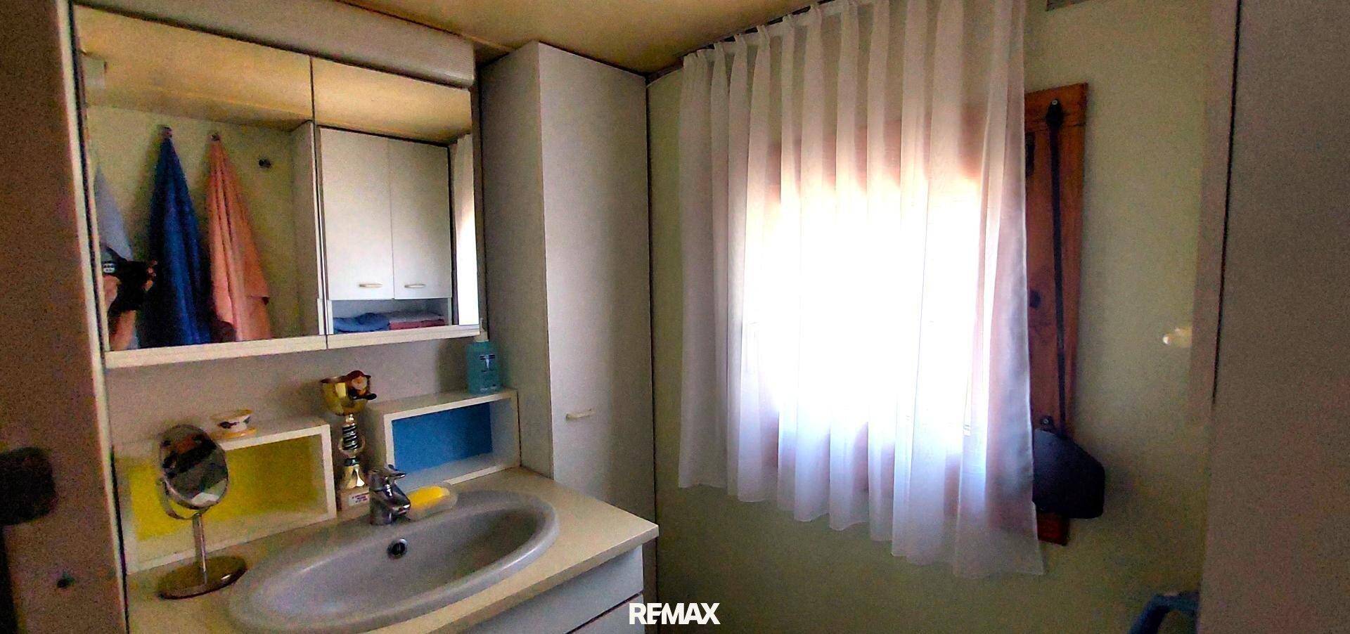 Badezimmer mit Waschbecken, Spiegelschrank und einem Fenster, das für Belüftung und Tageslicht sorgt.