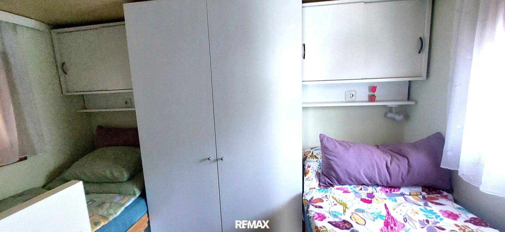 Schlafzimmer mit zwei Einzelbetten, einem weißen Kleiderschrank und praktischen Hängeschränken über den Betten.