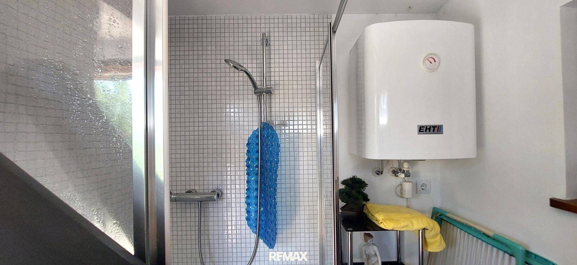 Duschbereich mit weißen Mosaikfliesen und einem an der Wand montierten Warmwasserbereiter.