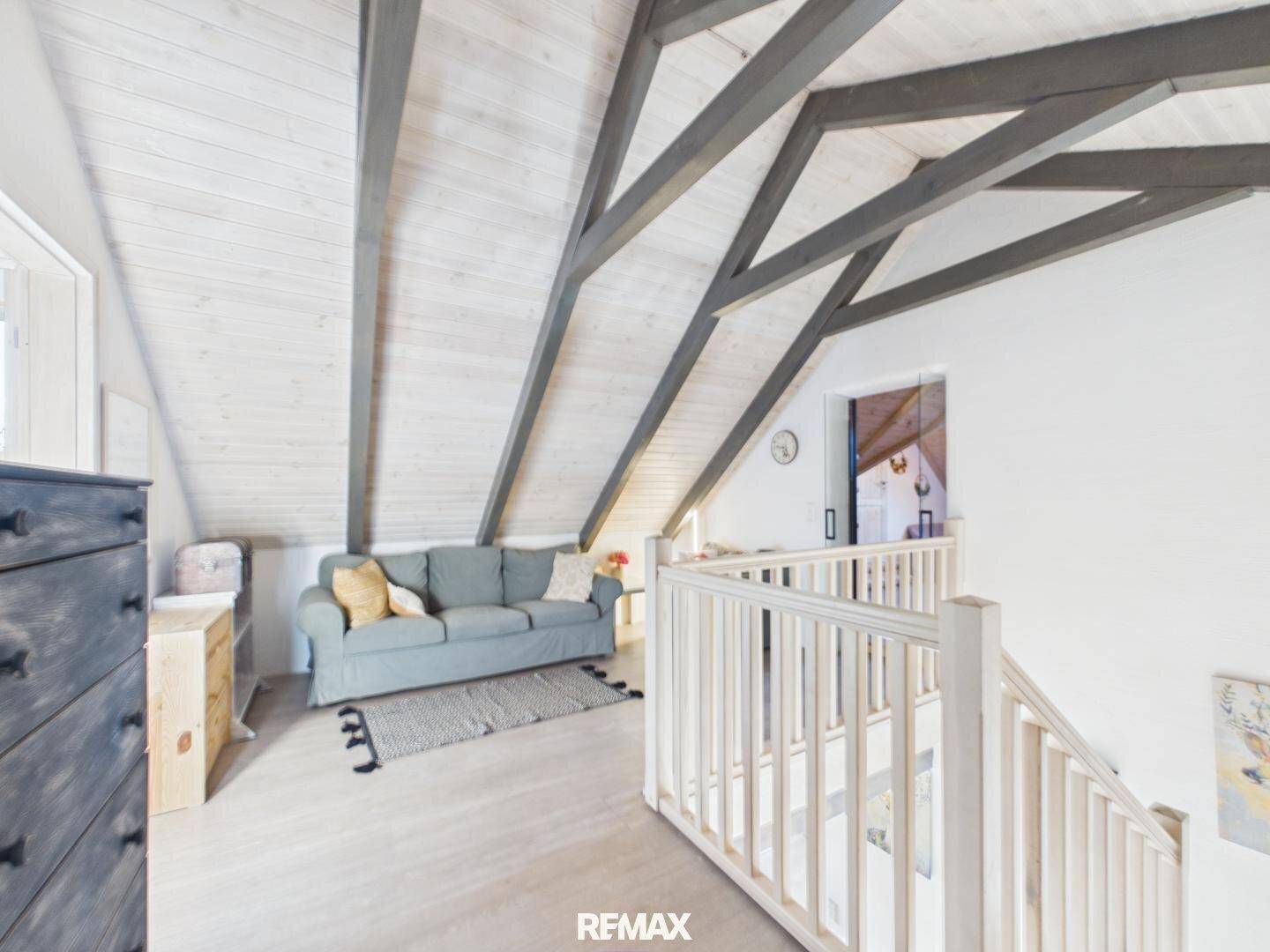 Ausgebauter Dachboden als Wohnbereich mit Sofa, sichtbaren Holzbalken und heller Holzvertäfelung.