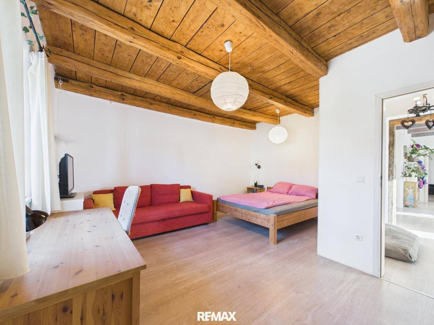 Gemütliches Schlafzimmer mit Holzdachschräge, Holzbalken und hellem Laminatboden.