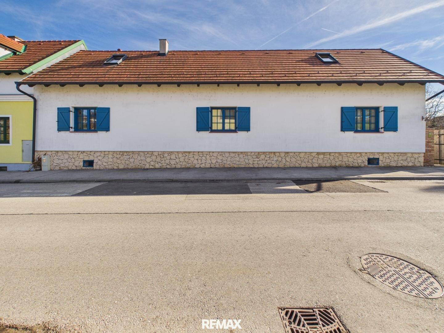 Traditionelle Hausfassade mit weißen Wänden, blauen Fensterläden und rotem Ziegeldach.