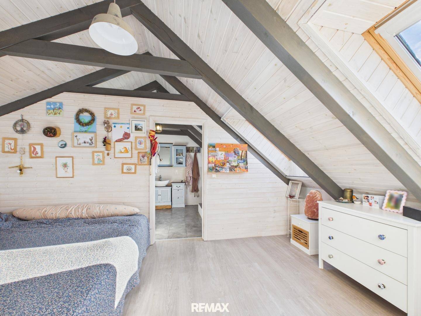 Helles Dachzimmer mit schrägen Wänden, sichtbaren Holzbalken und einem Dachfenster.