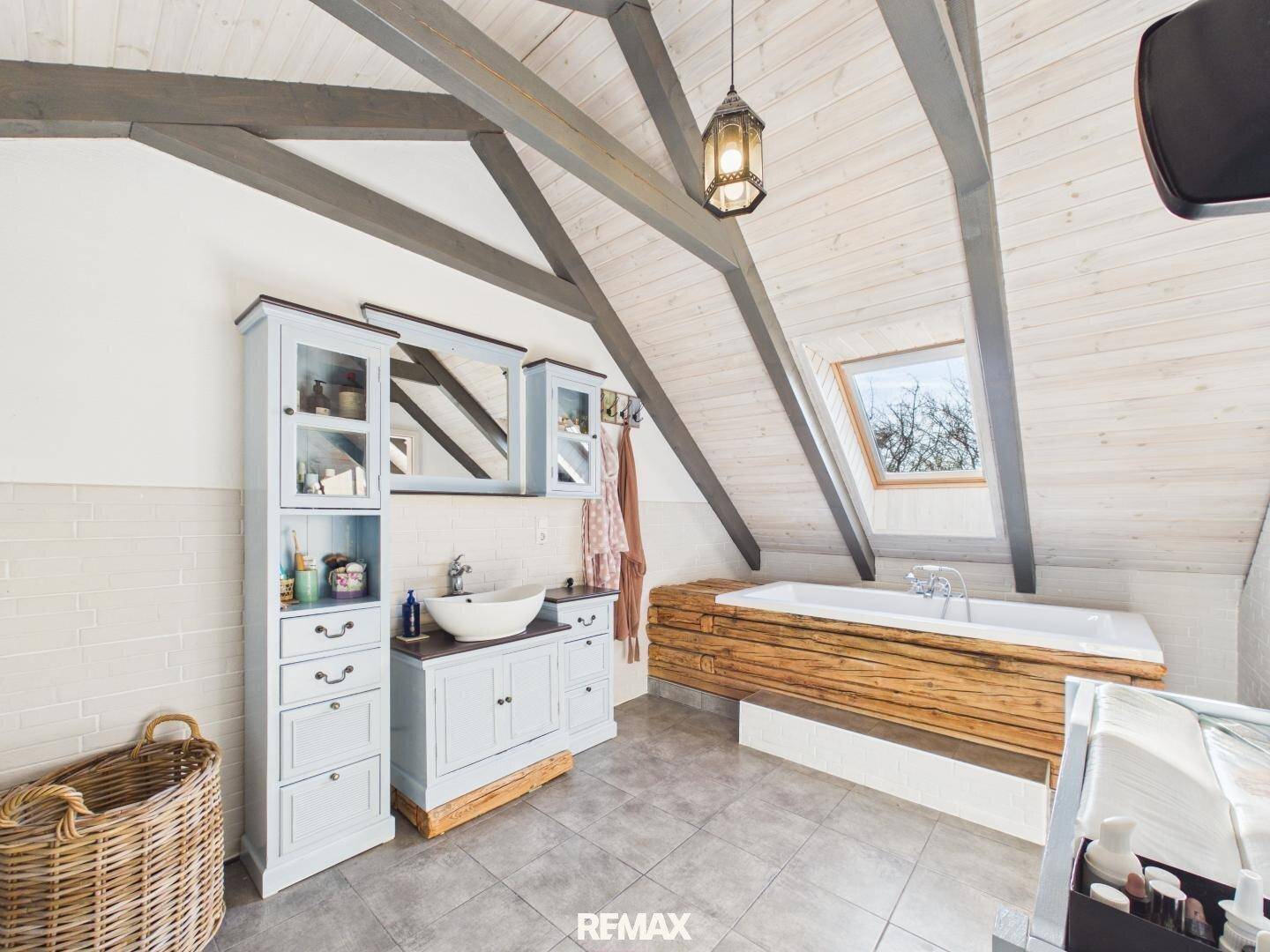 Dachgeschoss-Badezimmer mit freistehender Badewanne, Waschtisch und schräger Holzbalkendecke.