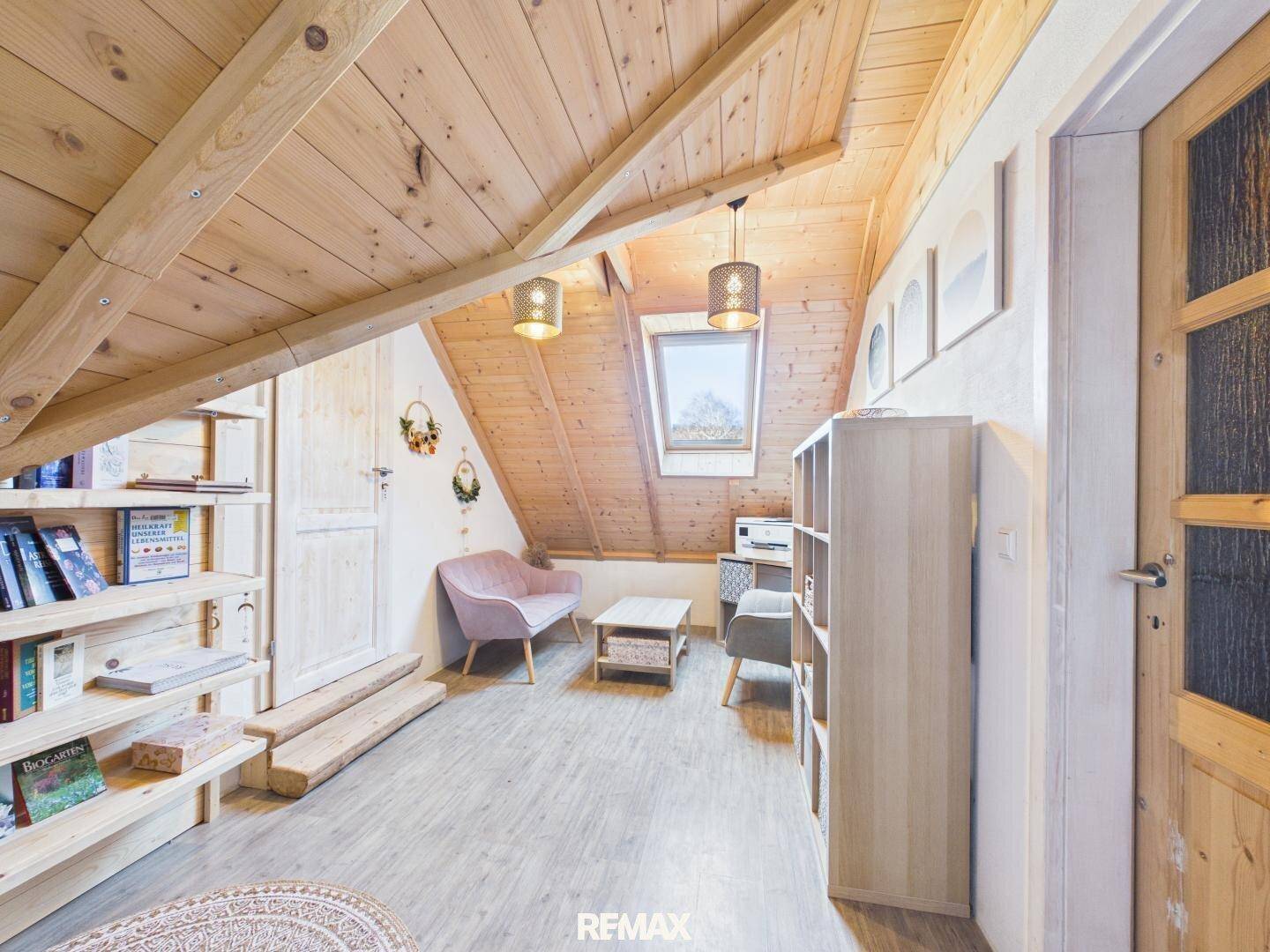 Gemütliches Dachzimmer mit Holzvertäfelung, kleiner Sitzecke und integrierten Bücherregalen.