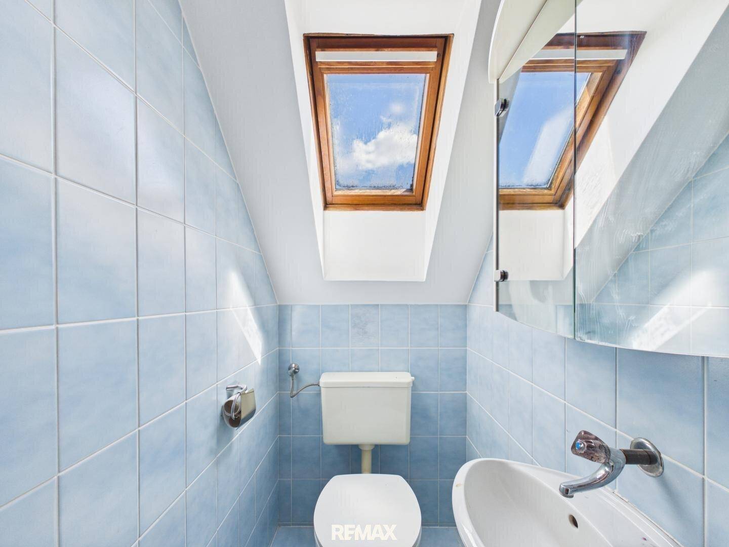 Kleines WC mit blauen Fliesen, Dachfenster und Waschbecken unter schräger Decke.