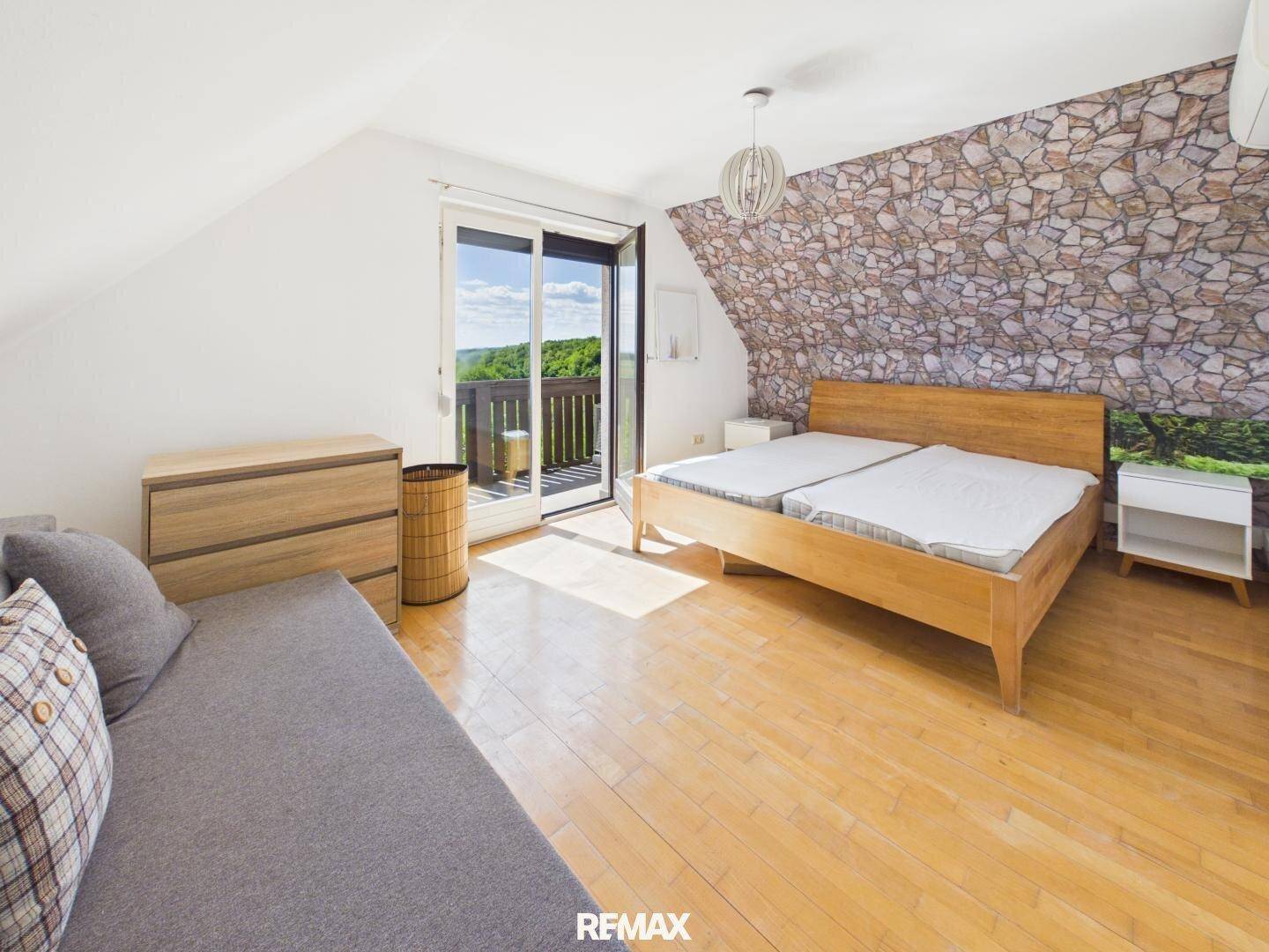 Geräumiges Schlafzimmer mit Holzbett, Parkettboden, Steinwand und Balkonzugang.