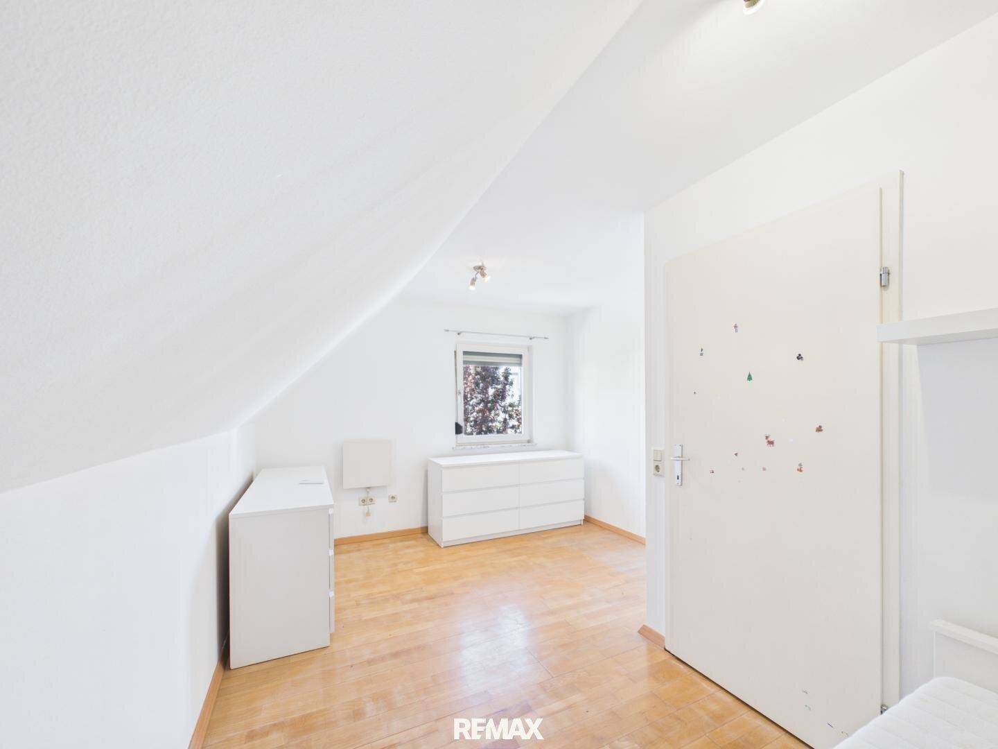 Helles Schlafzimmer mit Holzboden, weißen Wänden und schräger Decke im Dachgeschoss.