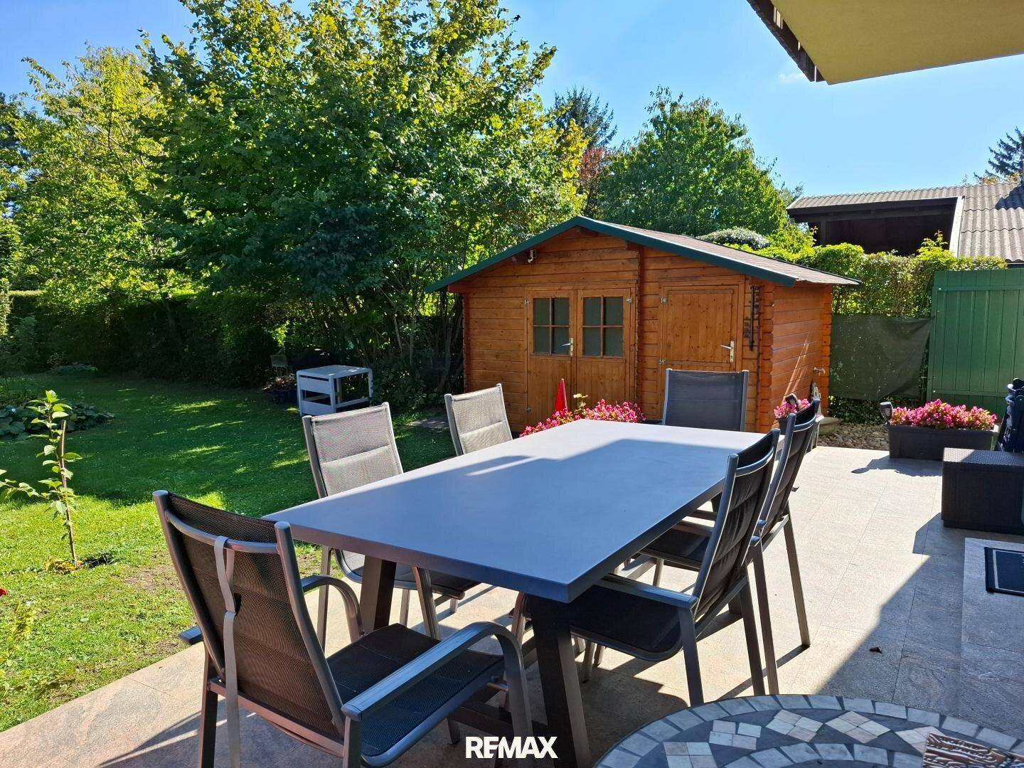 Geräumige Terrasse mit Esstisch und Blick auf den Garten mit Gartenhaus.