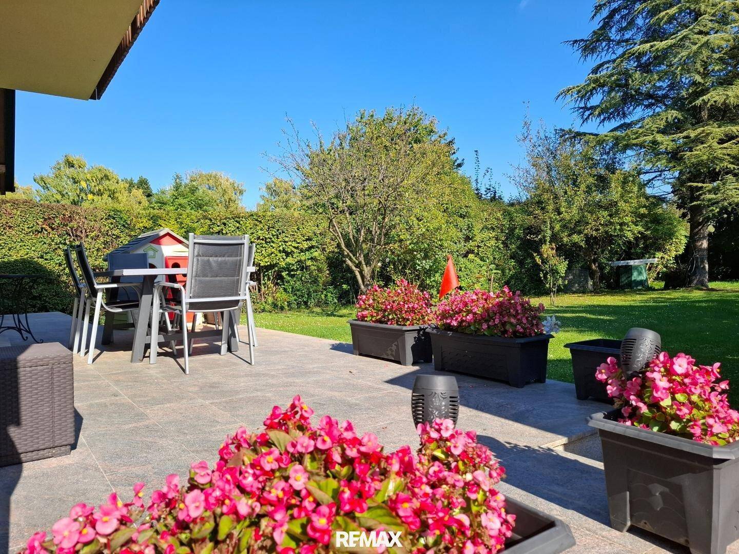 Sonniger Terrassenbereich mit Gartenmöbeln und Blumenbeeten.