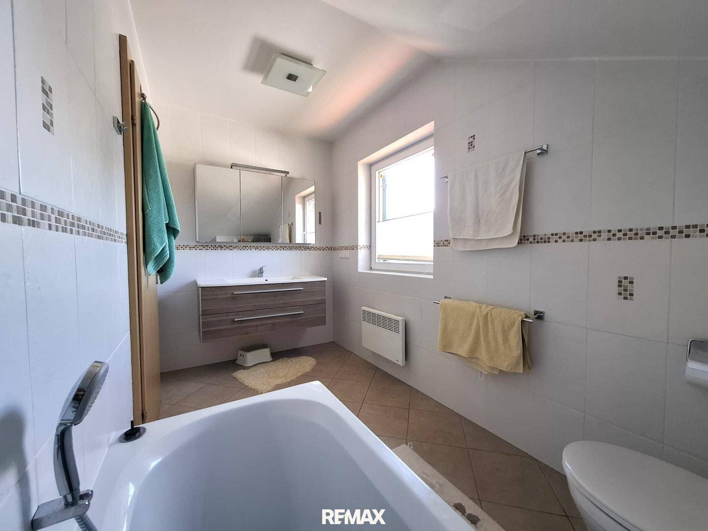 Geräumiges Badezimmer mit Badewanne, Waschbecken, WC und Fenster.